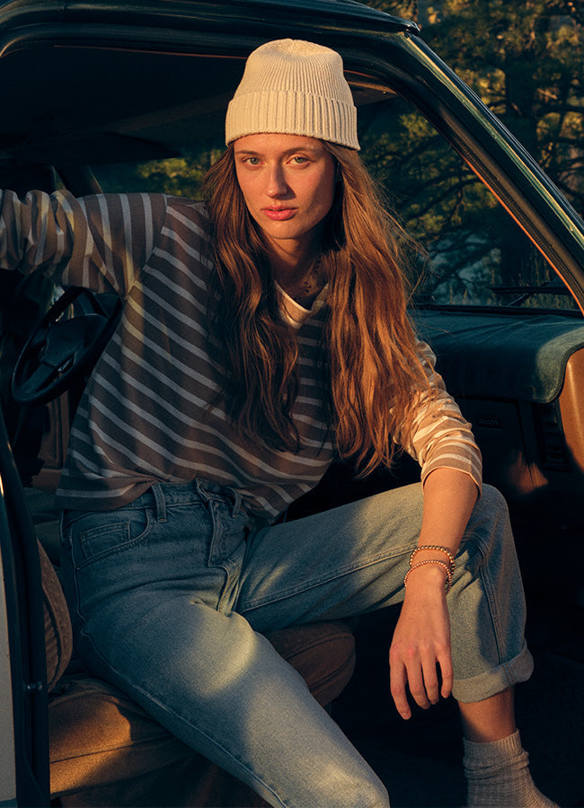 Woman wearing cream colored beanie, grey striped long sleeve top and jeans